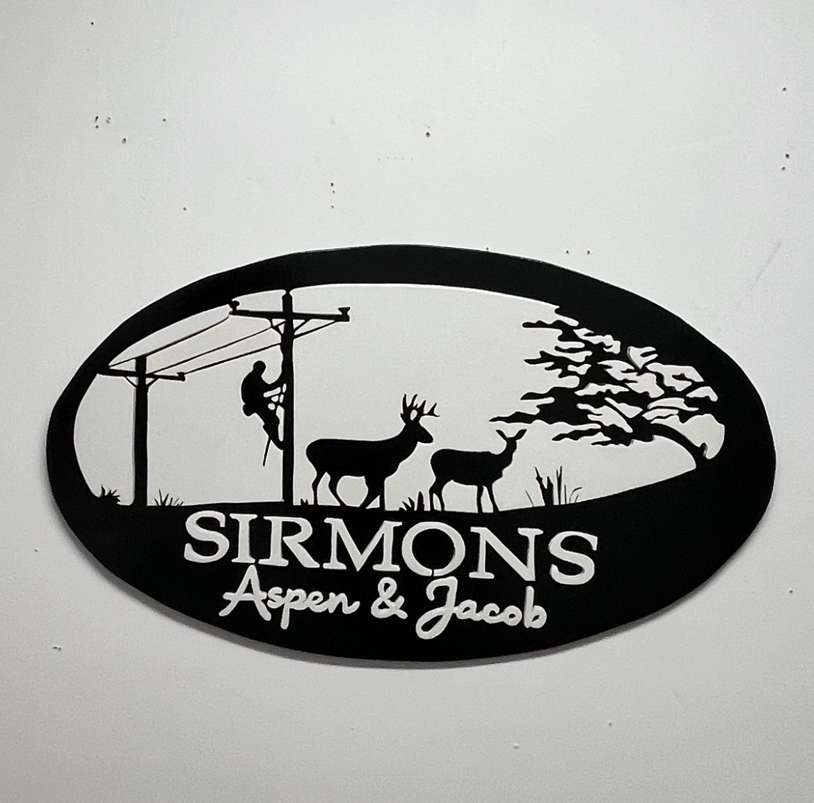'Sirmons' oval family sign with a lineman on the pole, two deer and a cut-out treeline