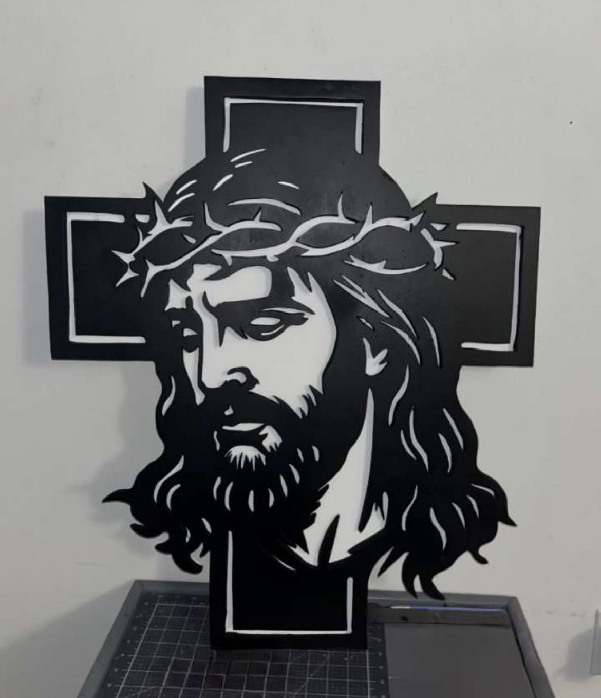 Face of Christ cross in flat black, the whole portrait formed by hand-cut negative space with the crown of thorns worked into the arms, example of custom handmade wood work