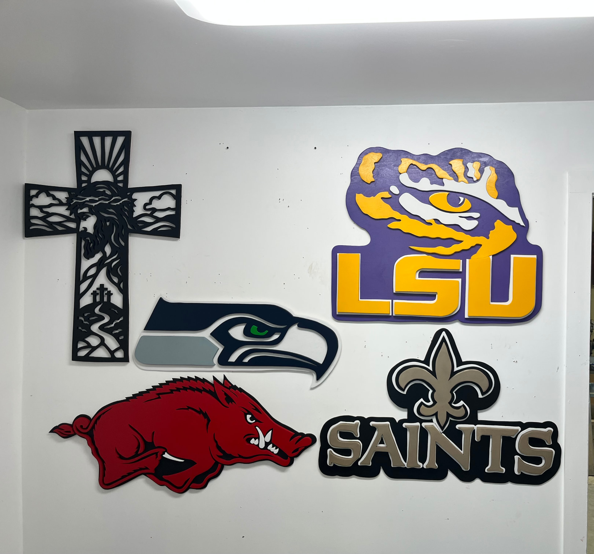 Finished wooden signs on the shop wall, including a cross, team logos and a Razorback