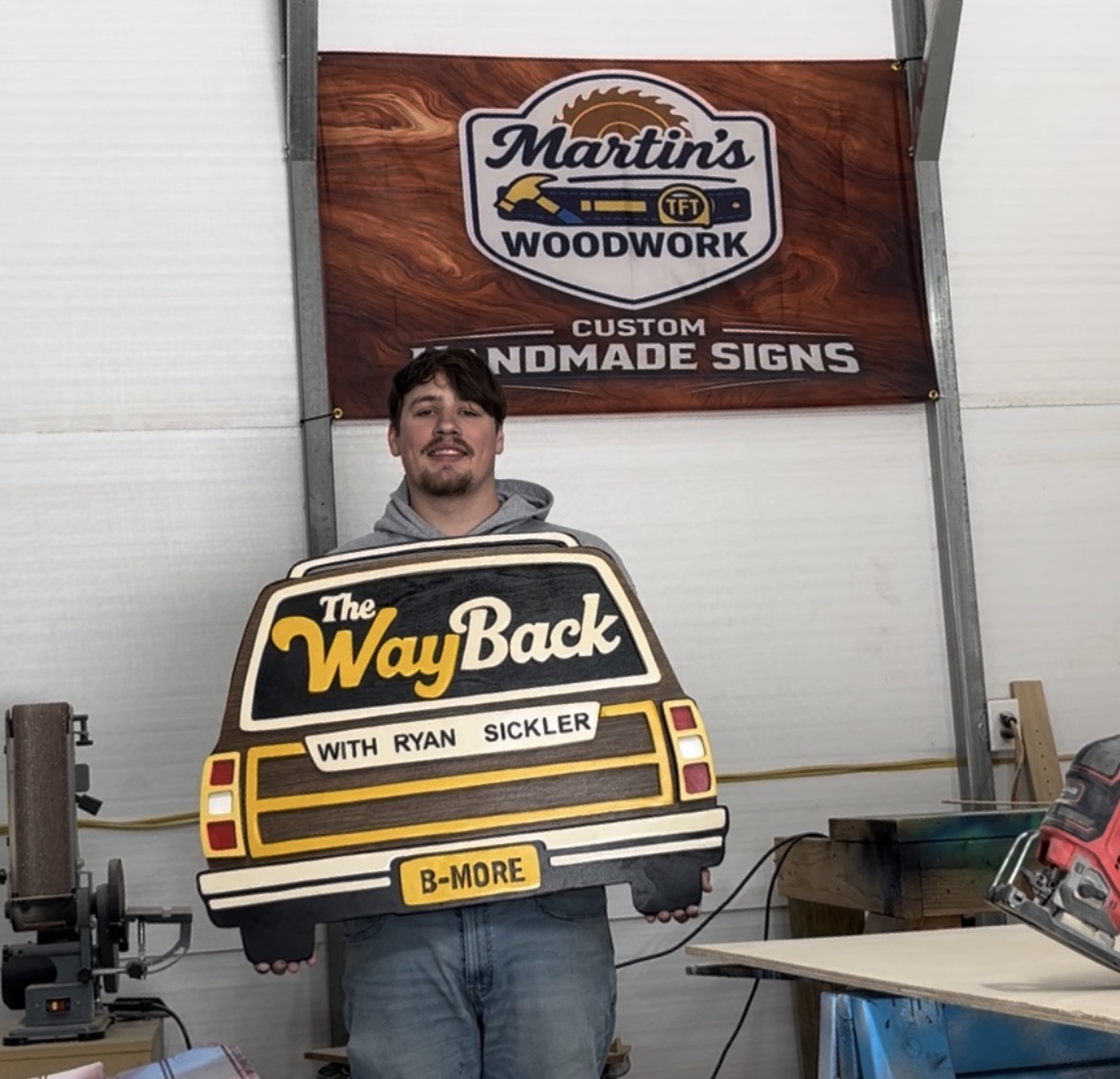 Dylan holding a finished hand-cut wooden sign in the shop